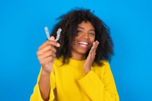 Happy MODEL holding and showing at camera an invisible aligner while laughing. Dental healthcare and confidence concept.